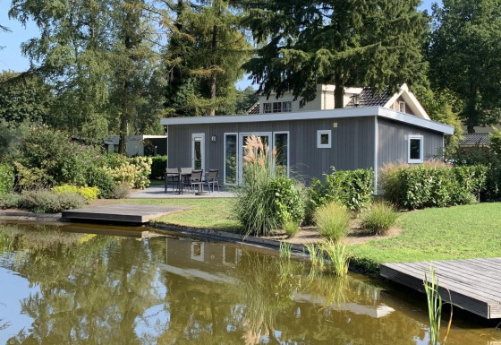 Pavilion 4 Lodge mit modernem grauem Design, umgeben von Grün und einem Teich im Vordergrund.