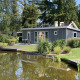 Pavilion 4 lodge med moderne gråt design, frodige omgivelser og en lille sø i forgrunden.