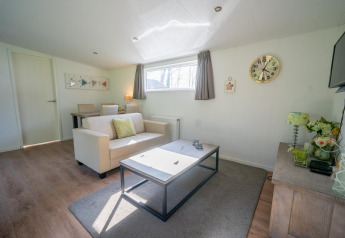Lichte woonkamer in Pavilion 4 bij De Achterhoek, Nederland, met bank, tafel en wandklok.