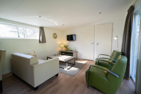 Stilfuld stue i Pavilion 4 på De Achterhoek i Holland med moderne møbler, lyst interiør og grønne stole.