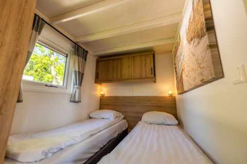 Habitación con dos camas individuales, armario de madera y ventana en Tiny House 4, De Achterhoek, Países Bajos.