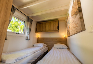 Habitación con dos camas individuales, armario de madera y ventana en Tiny House 4, De Achterhoek, Países Bajos.