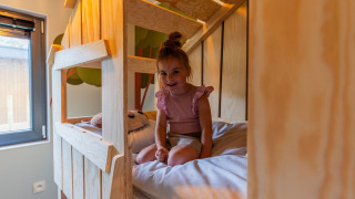 Niña sentada sobre una litera de madera en Kids Cottage, Kaatsheuvel, Países Bajos, disfrutando la estancia.