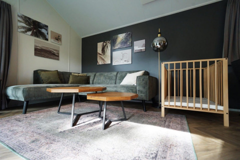 Sala de estar en la Baby Cottage lodge, con sofá verde, cuna de madera, mesas y arte en la pared.