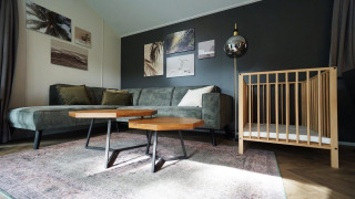 Sala de estar en la Baby Cottage lodge, con sofá verde, cuna de madera, mesas y arte en la pared.