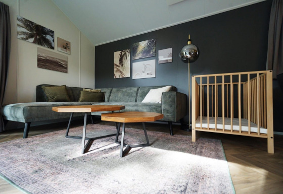 Sala de estar en la Baby Cottage lodge, con sofá verde, cuna de madera, mesas y arte en la pared.