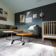 Stue i Baby Cottage-lodgen, med grøn sofa, træbabyseng, sofaborde og vægkunst på mørk væg.