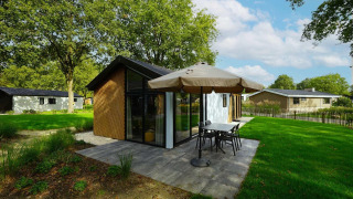 Moderne babyhytte i Kaatsheuvel, Holland, med terrasse, parasol og grønne omgivelser i solen.