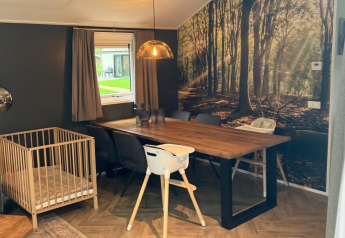 Sala da pranzo al Baby cottage di Kaatsheuvel, Paesi Bassi, con lettino, tavolo e murale di foresta.