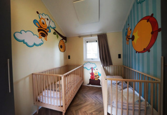 Børneværelse med to tremmesenge, farverige vægmalerier af bier og skyer i Baby Cottage, Kaatsheuvel.