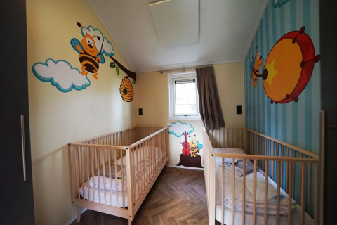 Stanza per bambini con due lettini e murales di api colorate al Baby Cottage a Kaatsheuvel, Paesi Bassi.