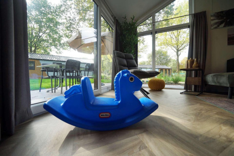 Cavallo a dondolo blu nel soggiorno di un cottage, porte a vetri con vista su patio e giardino a Kaatsheuvel.