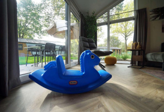 Caballito balancín azul en sala de cabaña, puertas de cristal con vista al jardín en Baby cottage, Kaatsheuvel.
