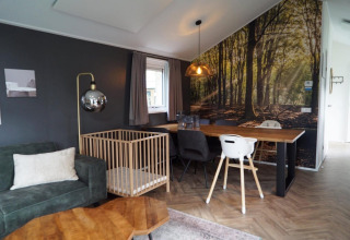Sala moderna en Baby Cottage Kaatsheuvel, Países Bajos, con mural de bosque, corralito y mesa de comedor.