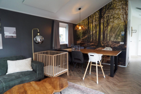 Sala moderna en Baby Cottage Kaatsheuvel, Países Bajos, con mural de bosque, corralito y mesa de comedor.