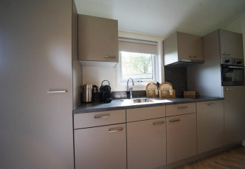 Moderne keuken in de Baby cottage lodge te Kaatsheuvel, Nederland, met grijze kasten en een raam.