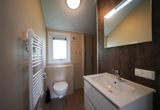 Baño moderno con lavabo, espejo, inodoro y radiador en Baby cottage en Kaatsheuvel, Países Bajos.