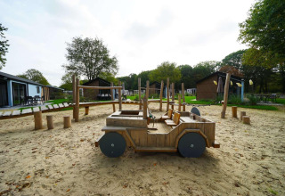 Parque infantil con coche de madera y arena en Baby Cottage lodge en Kaatsheuvel, Países Bajos, rodeado de cabañas.