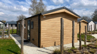 Modern Berkel lodge with wooden exterior, surrounded by small gardens under a blue sky with clouds.