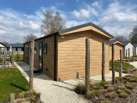 Lodge Berkel moderno de exterior de madera, rodeado de pequeños jardines y cielo azul con nubes.