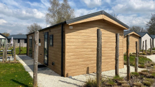 Lodge Berkel moderno de exterior de madera, rodeado de pequeños jardines y cielo azul con nubes.