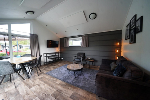 Sala de estar moderna en la cabaña Berkel en Kaatsheuvel, Países Bajos, con sofá y ventanas grandes.