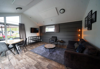 Sala de estar moderna en la cabaña Berkel en Kaatsheuvel, Países Bajos, con sofá y ventanas grandes.