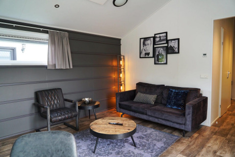 Interior moderno de glamping en Berkel con sofá, sillón, mesa de centro y fotos decorativas en la pared.