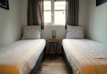 Deux lits simples dans un hébergement glamping à Berkel avec une petite table et une lampe entre eux.