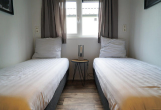 To enkeltsenge på et glampingophold ved Berkel med et lille bord og en lampe mellem sengene.