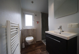 Baño moderno en la cabaña Berkel en Kaatsheuvel, Países Bajos, con ducha, inodoro, lavabo y ventana.