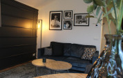 Salon confortable au glamping Berkel avec canapé sombre, tableaux muraux, lampe moderne et tables en bois.