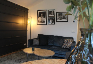 Gezellige Berkel glamping woonkamer met donkere zetel, kunst aan de muur, moderne lamp en houten tafels.