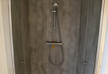 Doccia moderna con pareti effetto cemento e soffione a pioggia al lodge Berkel a Kaatsheuvel, Paesi Bassi.