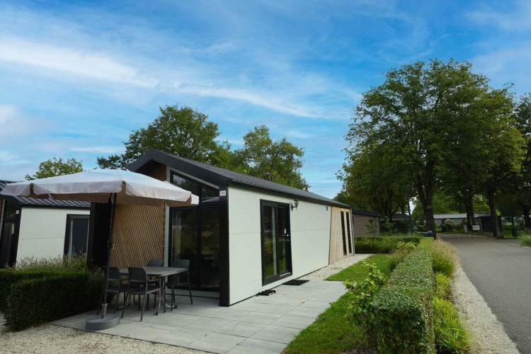 Modern lodge with a patio and umbrella at Berkel in Kaatsheuvel, Netherlands, surrounded by greenery.