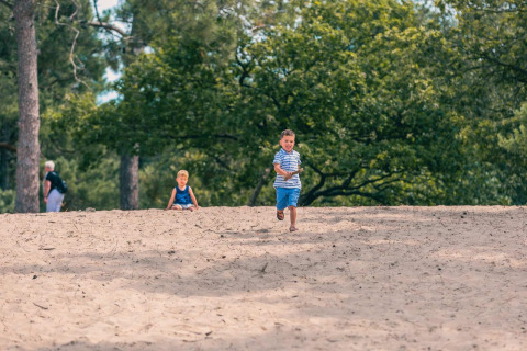 Dos niños juegan en la arena frente a árboles en Pavilion Maximaal, Kaatsheuvel, Países Bajos, en un día soleado.