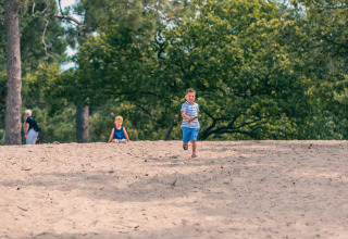 Dos niños juegan en la arena frente a árboles en Pavilion Maximaal, Kaatsheuvel, Países Bajos, en un día soleado.