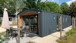 Modern Berkel lodge with patio, dining table, and umbrella, surrounded by greenery and peaceful nature.