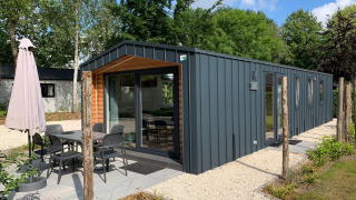 Moderne Berkel-Lodge mit Terrasse, Esstisch und Sonnenschirm in einer grünen, ruhigen Umgebung.