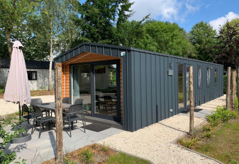 Moderne Berkel lodge met terras, eettafel en parasol omgeven door rust en veel groen.