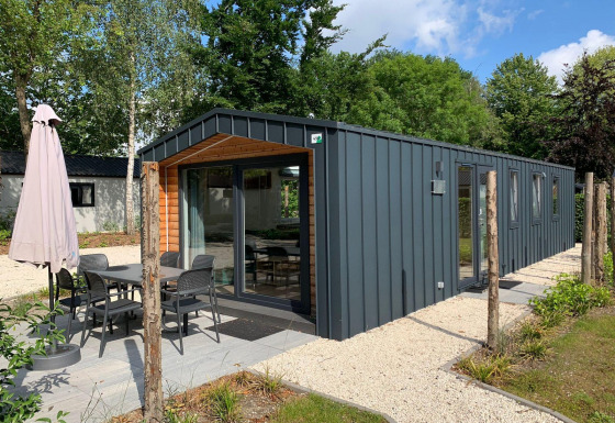 Moderne Berkel-Lodge mit Terrasse, Esstisch und Sonnenschirm in einer grünen, ruhigen Umgebung.