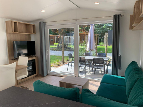 Wohnbereich der Berkel-Lodge in Kaatsheuvel, Niederlande, mit grünem Sofa, TV und Terrasse mit Sitzgruppe.