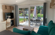 Wohnbereich der Berkel-Lodge in Kaatsheuvel, Niederlande, mit grünem Sofa, TV und Terrasse mit Sitzgruppe.