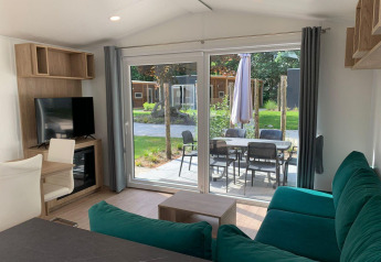 Woonkamer van lodge Berkel in Kaatsheuvel, Nederland, met groene zetel, tv en zicht op terras via schuifdeur.