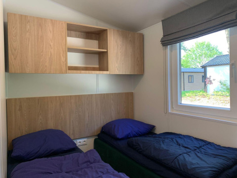 Habitación con dos camas individuales, ropa de cama azul, armarios de madera y ventana en Berkel, Kaatsheuvel.