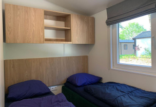 Habitación con dos camas individuales, ropa de cama azul, armarios de madera y ventana en Berkel, Kaatsheuvel.