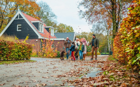 Familie spaziert mit Hund vor der Berkel-Lodge in Kaatsheuvel, Niederlande, umgeben von Herbstlaub.