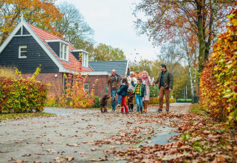 Familie wandelt met hond voor lodge Berkel in Kaatsheuvel, Nederland, te midden van herfstkleuren.