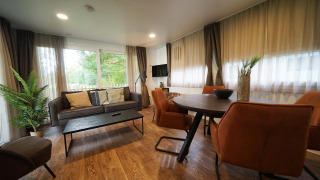 Acogedora sala de estar en cabaña con grandes ventanales, sofá marrón y mesa de comedor redonda.
