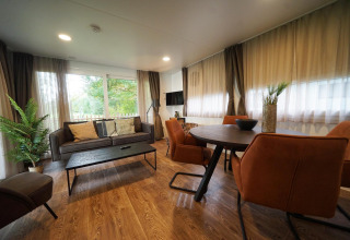 Modern lodge living area with large windows, comfortable sofa, round dining table, and greenery decor.
